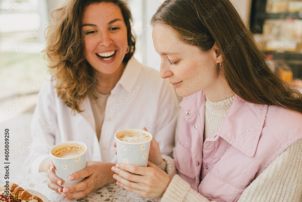 Two friends sitting near window in a coffeehouse, enjoying coffee, laughing and chatting. Two friends sitting near window in a coffeehouse, enjoying coffee, laughing and chatting.