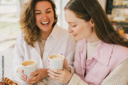 Two friends sitting near window in a coffeehouse  enjoying coffee  laughing and chatting.
