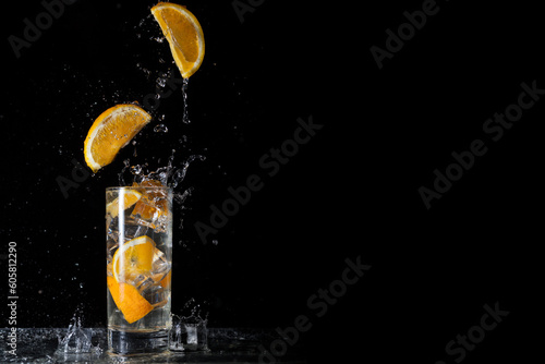 Cool and fresh drink of orange lemonade with orange slices and ice on a black background with falling orange slices and ice