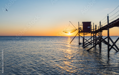 A fishing hut called carrelet with craft lifting net at sunset. Esnandes, charente maritime, France. The sun is caught in the net.