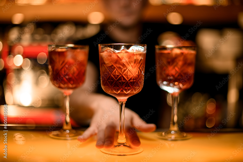 Hand of bartender serving fresh red cocktail with ice cubes in a glass on the bar counter in the bar