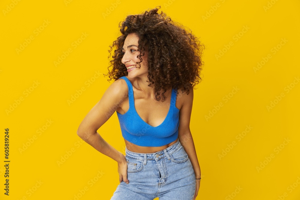 Woman with curly afro hair in a blue t-shirt on. yellow background signs with her hands, look into the camera, smile with teeth and happiness, copy space Woman with curly afro hair in a blue t-shirt on. yellow background signs with her hands, look into the camera, smile with teeth and happiness, copy space