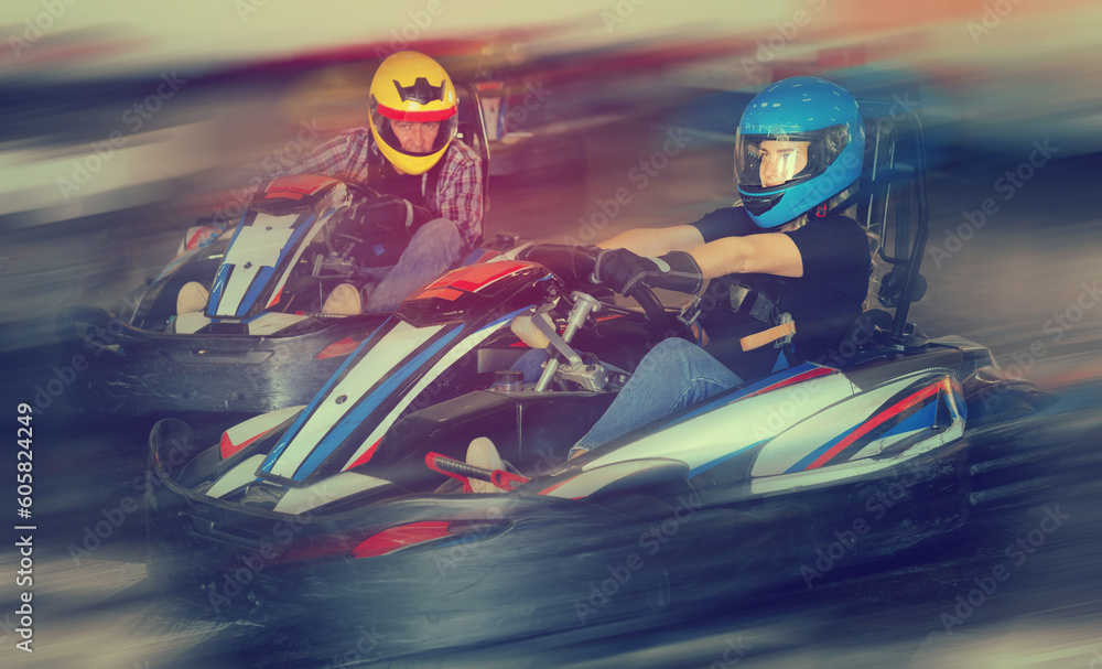 Group of nice male and females in helmets driving racing cars at kart track.