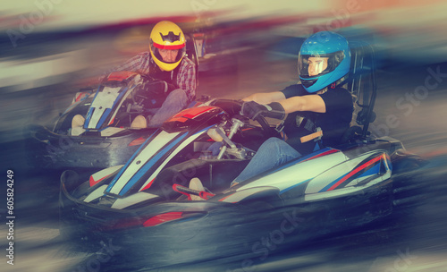 Group of nice male and females in helmets driving racing cars at kart track. © JackF