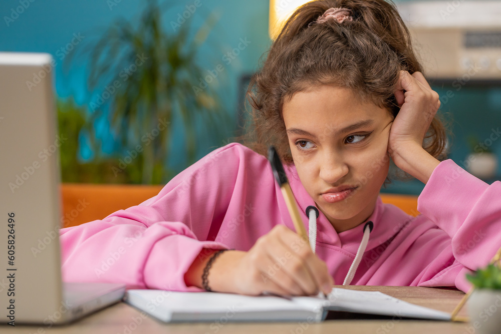 Bored tired Caucasian preteen school girl doing homework exercise online, typing on laptop, makes notes in notebook. Distance learning education. Young child kid at home workplace sitting at the table Bored tired Caucasian preteen school girl doing homework exercise online, typing on laptop, makes notes in notebook. Distance learning education. Young child kid at home workplace sitting at the table