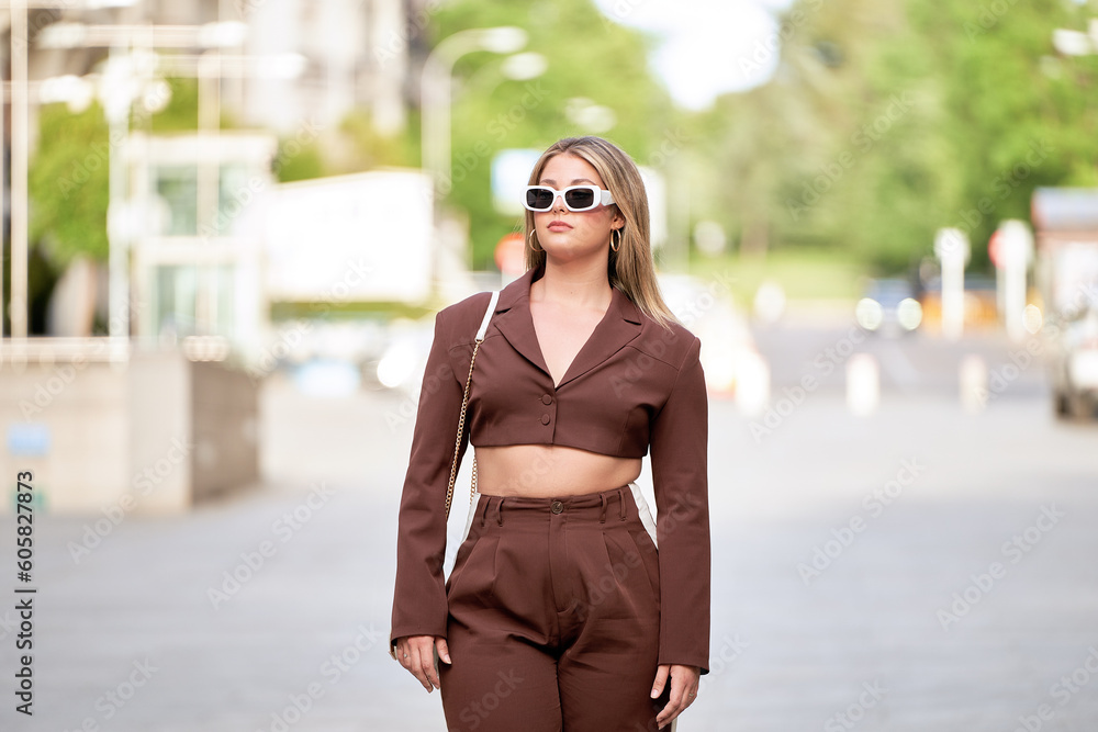 Young blonde girl with sunglasses enjoying a stroll through the city streets, radiating style and confidence.