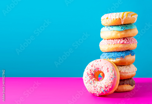 Sweet donuts of different bright colors lie in a large pile on a colored background