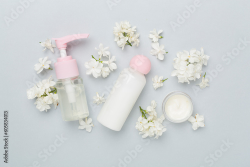 Composition with cosmetic bottles and flowers on color background, top view
