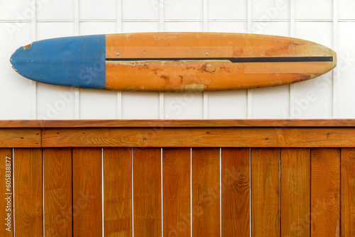 Old surfboard mounted on wall above fence.