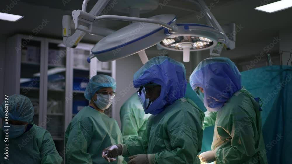 One surgeon of a big team turns to the nurse stretching hand for the instrument. Doctors in protective suits perform arthroscopic operation. One surgeon of a big team turns to the nurse stretching hand for the instrument. Doctors in protective suits perform arthroscopic operation.