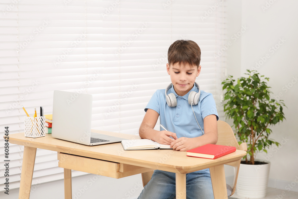Boy writing in notepad near laptop at desk in room. Home workplace Boy writing in notepad near laptop at desk in room. Home workplace