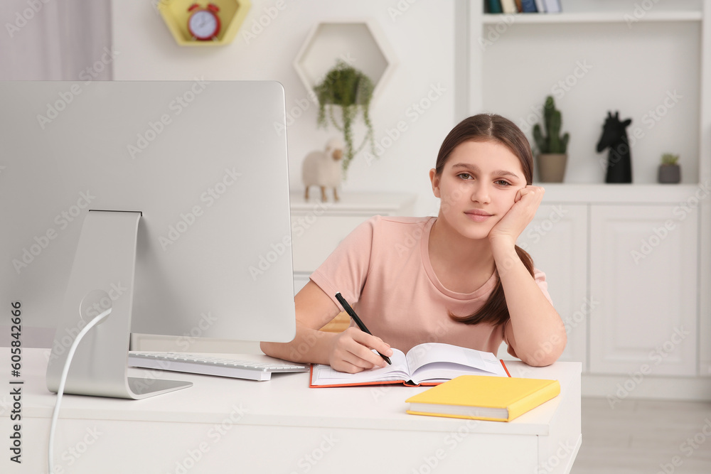 Tired girl writing in notepad while using computer at desk in room. Home workplace Tired girl writing in notepad while using computer at desk in room. Home workplace