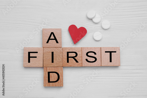 Words First Aid made of cubes, cardboard heart and pills on white wooden table, flat lay