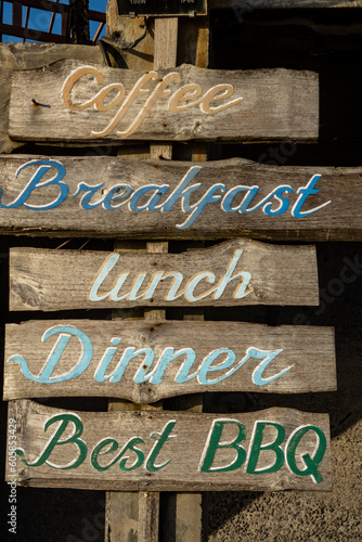 Canggu, Bali, Indonesia A wooden sign in Eglish offering breakfast, lunch, dinner, coffee, and best BBQ.