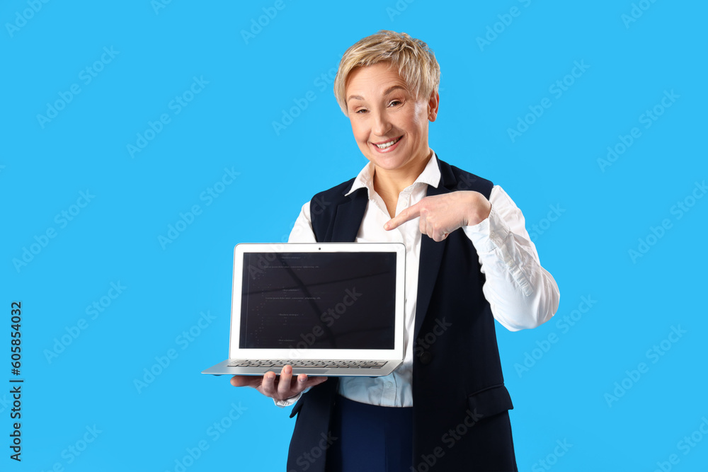 Mature female programmer pointing at laptop on blue background Mature female programmer pointing at laptop on blue background