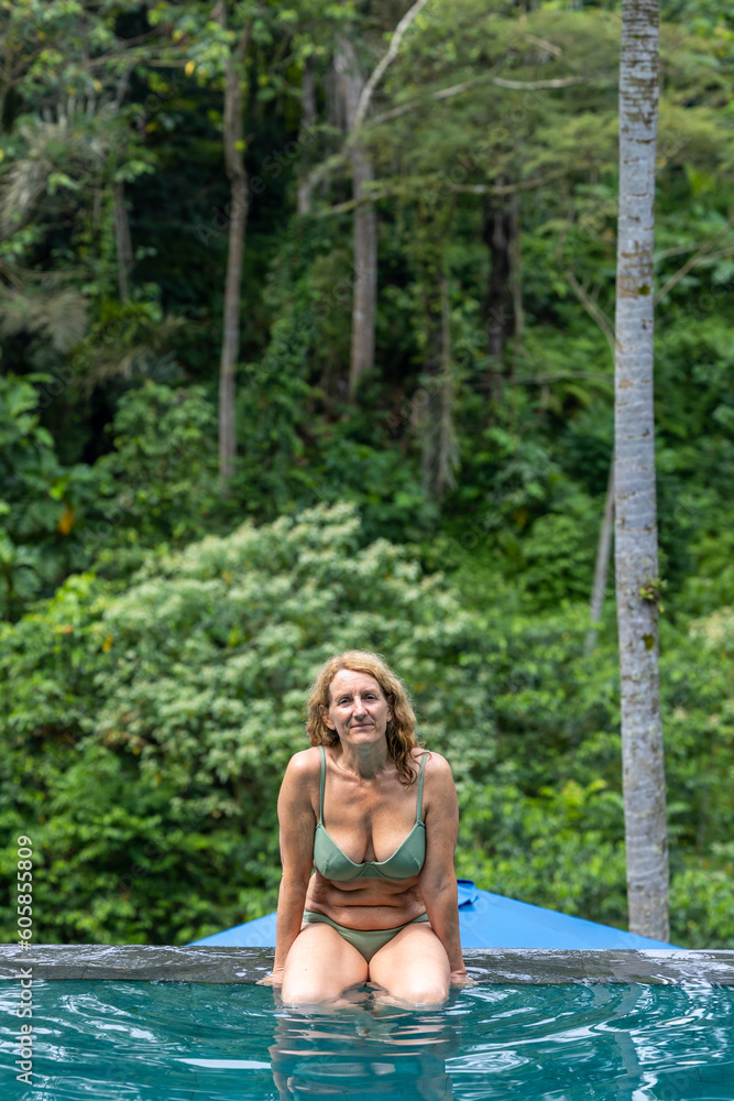 Ubud, Bali, Indonesia A woman sits on the edge of a pool with a jungle backdrop.