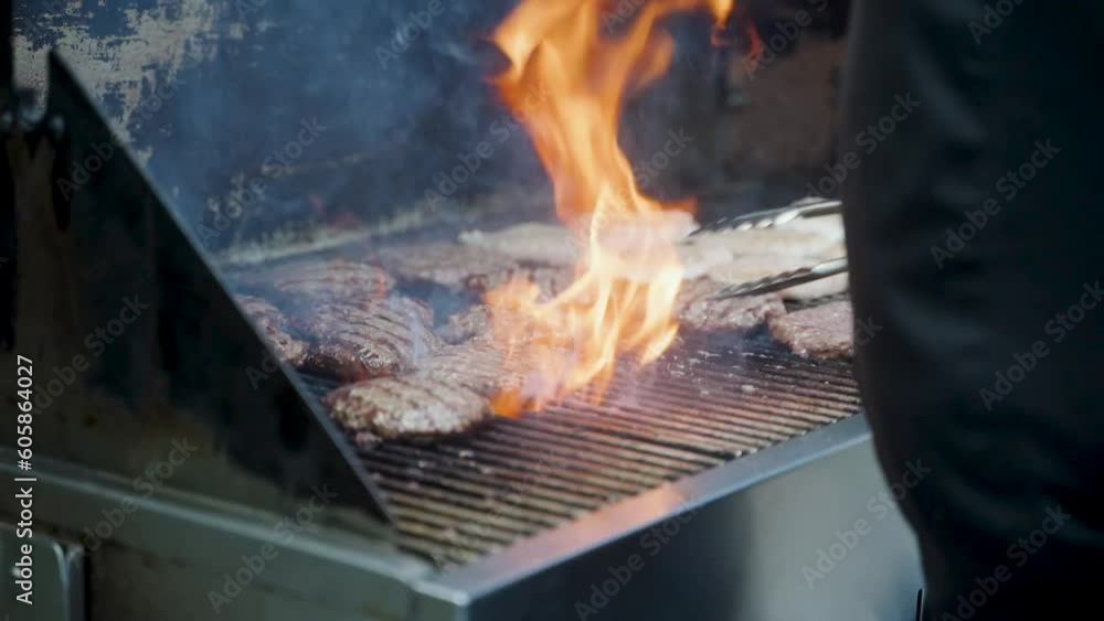 A chef flipping burgers between an open flame on a barbecue. A chef flipping burgers between an open flame on a barbecue.