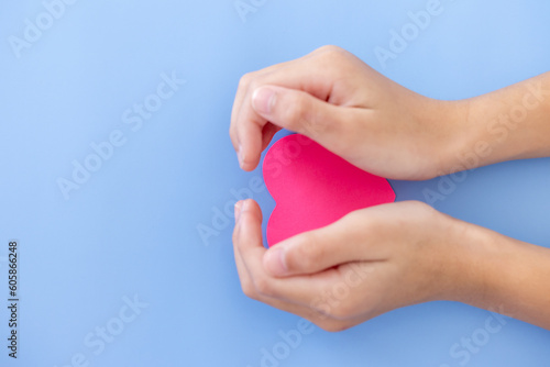 Closeup,Child's hands with a red heart on blue background.Give love philanthropy,help warmth and take care,protect children's health,blood donation and stem cell,valentines day concept.Space for text.