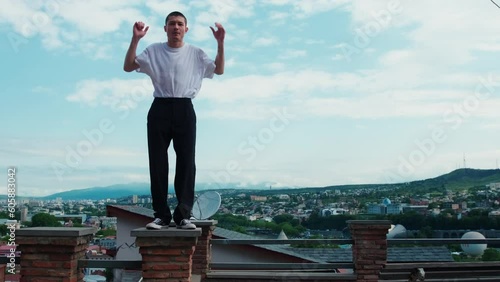 A guy in a white T-shirt is dancing a modern dance on the streets of the old city. Historical streets of Tbilisi. A young dancer improvises in a dance against a clear, blue sky. photo