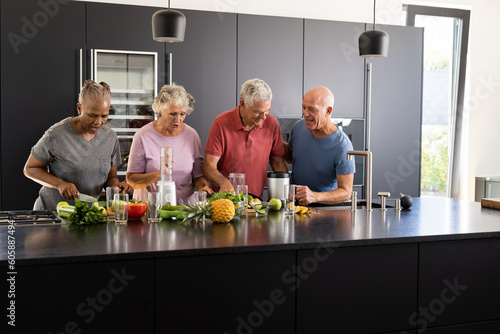 Happy diverse senior friends talking and preparing healthy smoothies together in kitchen