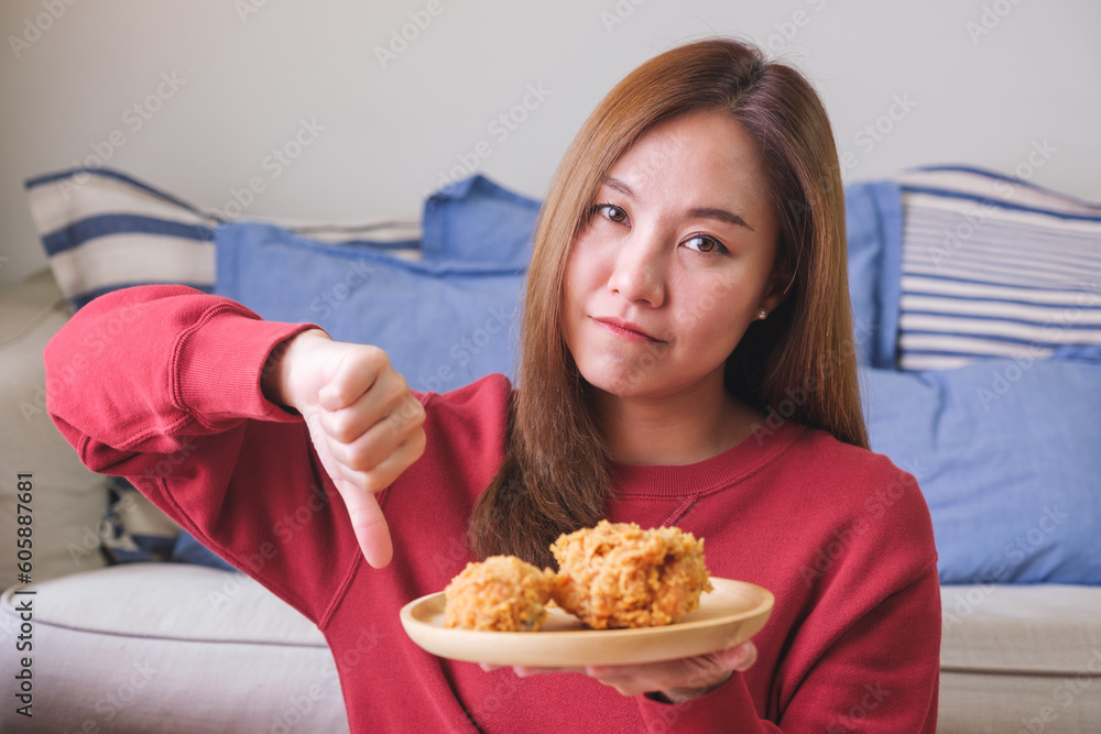 Portrait image of a young woman making thumb down hand sign while holding a plate of fried chicken