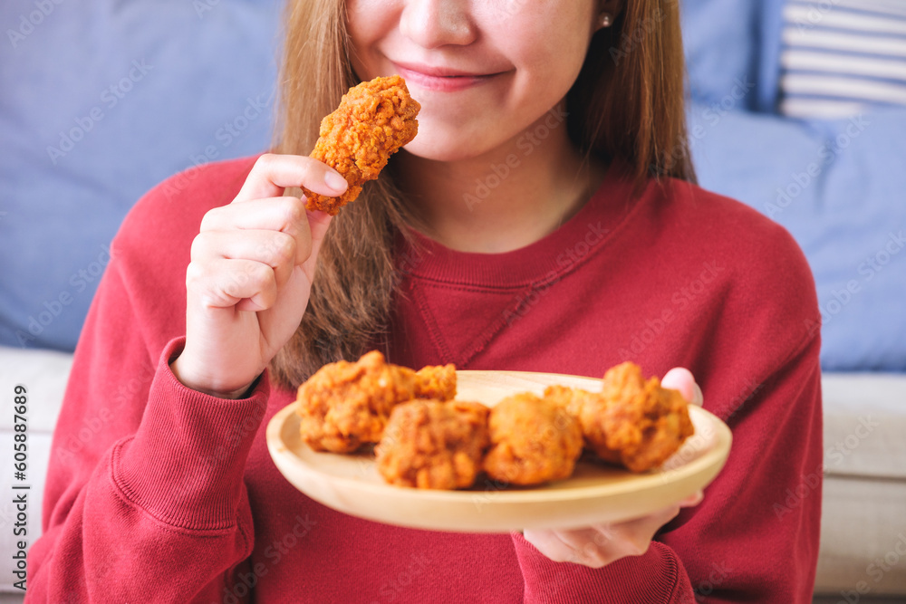 Closeup image of a young woman holding and eating fried chicken at home