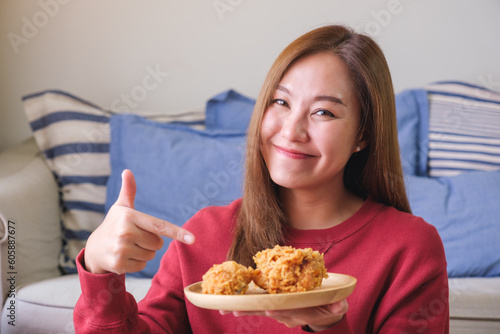 Portrait image of a woman holding and pointing finger at a plate of fried chicken