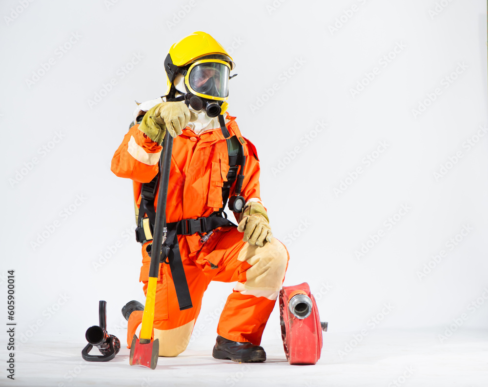 Naklejka premium Professional firefighter is sitting and kneeling down looking sideways and holding an iron axe with one hand while a fire hose is placed on the floor on a white background.