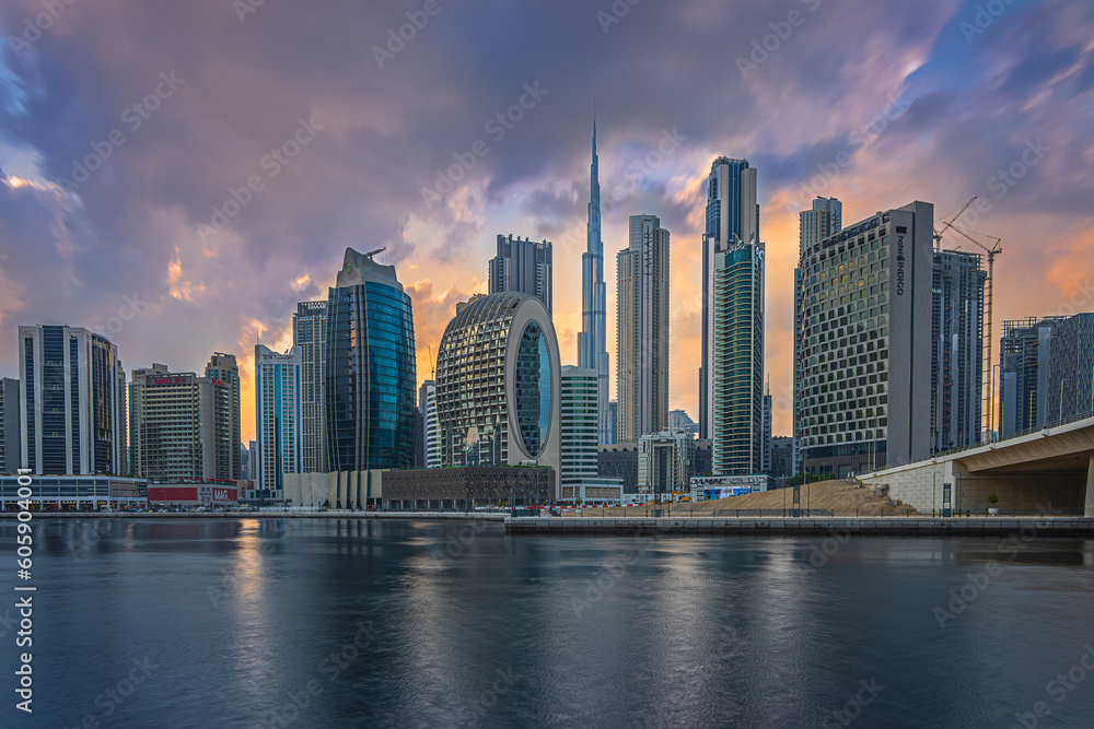 Mystical sunset with a cloudy sky over the skyline of the financial district in Dubai. Business center with office buildings and skyscrapers around Burj Khalifa. Street with a bridge over the harbor