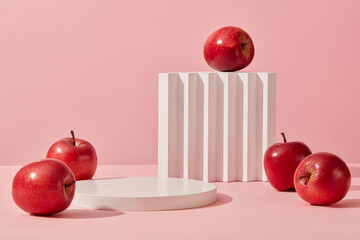 Some red apples displayed on a pink background with cylinder white podiums. Abstract background with minimalist style for product brand presentation. Advertising cosmetic from apple ingredient