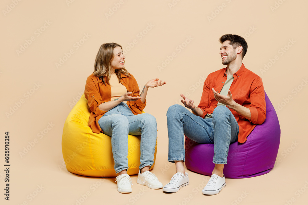 Full body smiling young couple two friends family man woman wear casual clothes together sit in bag chair talk speak spread hands isolated on pastel plain light beige color background studio portrait. - obrazy, fototapety, plakaty 