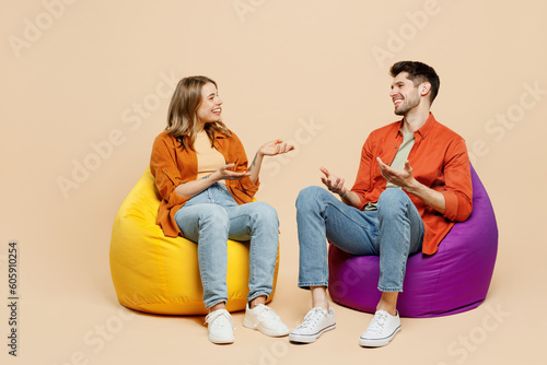 Bilde på lerret Full body smiling young couple two friends family man woman wear casual clothes together sit in bag chair talk speak spread hands isolated on pastel plain light beige color background studio portrait