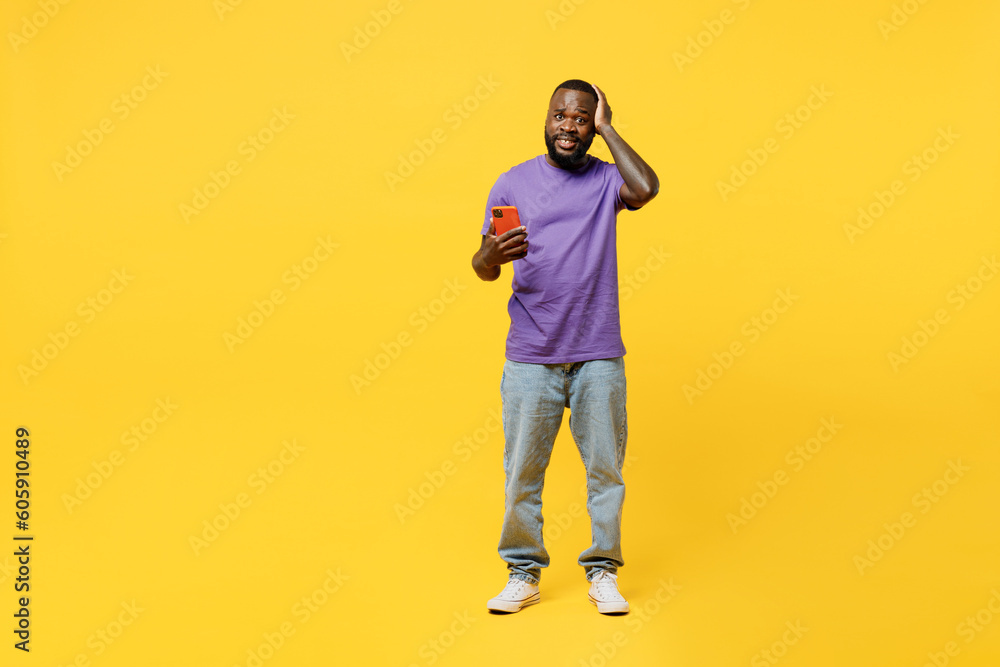 Fototapeta premium Full body young man of African American ethnicity wear casual clothes purple t-shirt hold head use mobile cell phone lok camera isolated on plain yellow background studio portrait. Lifestyle concept.