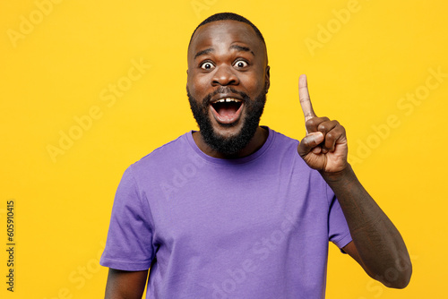 Young excited man of African American ethnicity he wear casual clothes purple t-shirt holding index finger up with great new idea isolated on plain yellow background studio portrait Lifestyle concept