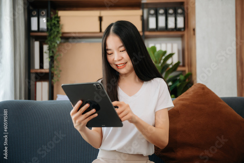 Asian woman using the smartphone and tablet on the sofa at home.
