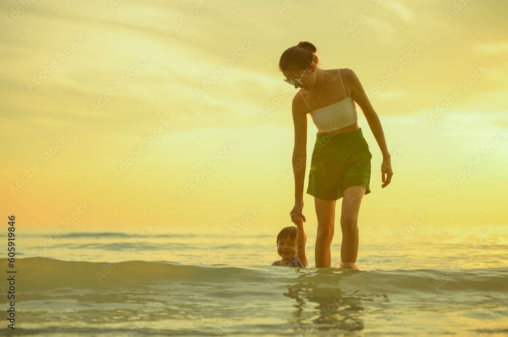 Happy family resting at beach in summer, Mother and baby boy feet at the sea foam at the sunlight water is moving