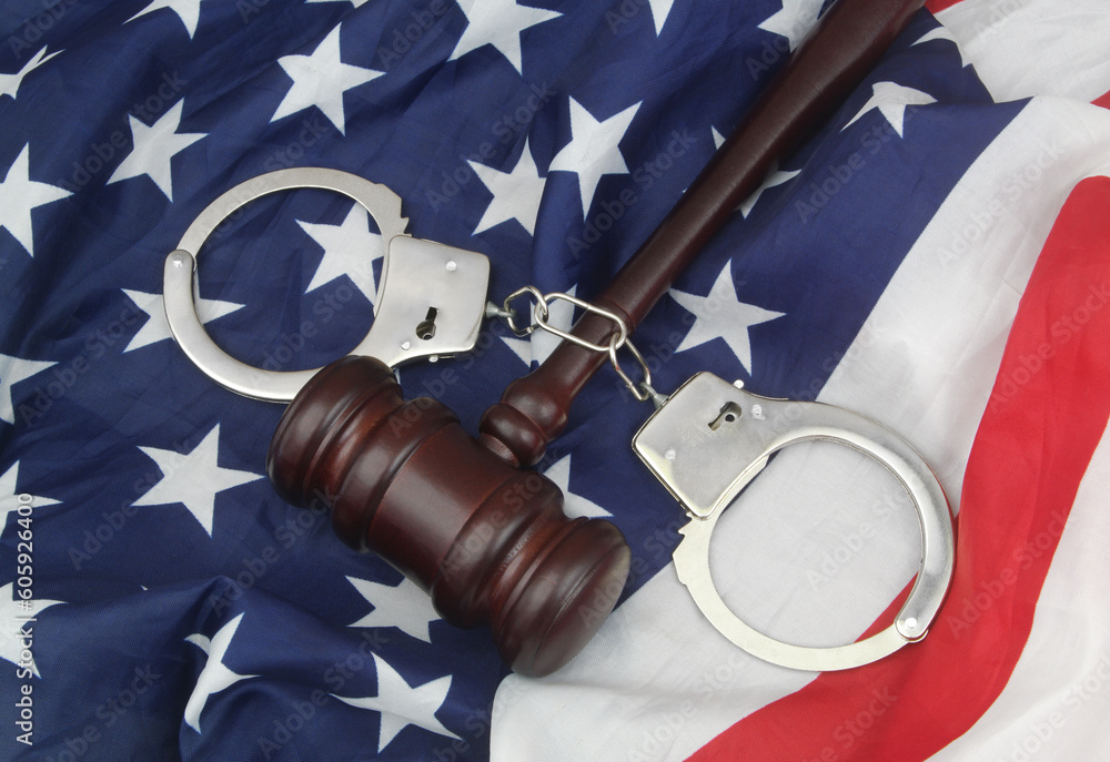 USA legal system and crimes concept. Judge wooden gavel and handcuffs on US flag.