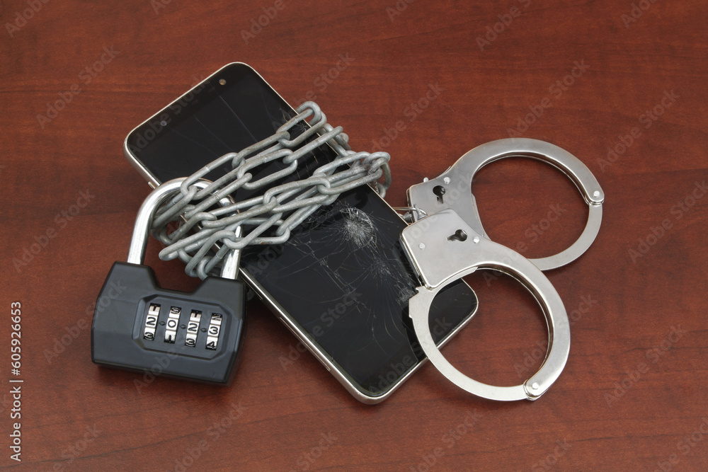 Obraz premium Chained smartphone by padlock with numbers 2023 and handcuffs. Cyber crime and punishments concept.