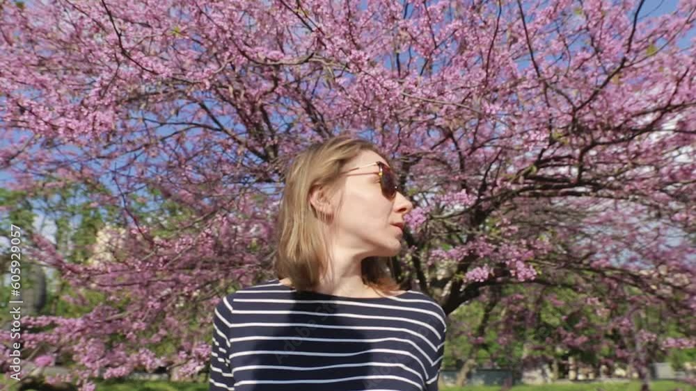 Video portrait middle aged woman in unglasses under the blooming sakura tree. Smiling, looking up aside and thinking. Video portrait middle aged woman in unglasses under the blooming sakura tree. Smiling, looking up aside and thinking.