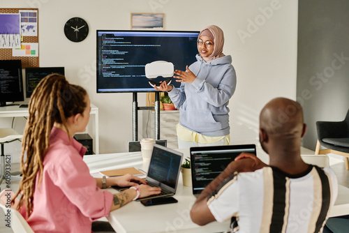 Young woman presenting new VR glasses to her colleagues during meeting in office