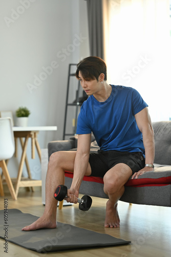 Millennial muscular male lifting dumbbell during morning workout at home. Fitness, weightlifting and bodybuilding concept