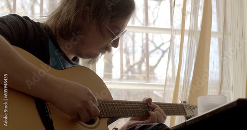 Mental exercise in free time. Make a melody. He puts chords by hand, creating music. Glasses eyes. Painted nails male musician plays guitar room near the window gratings opening frames. 