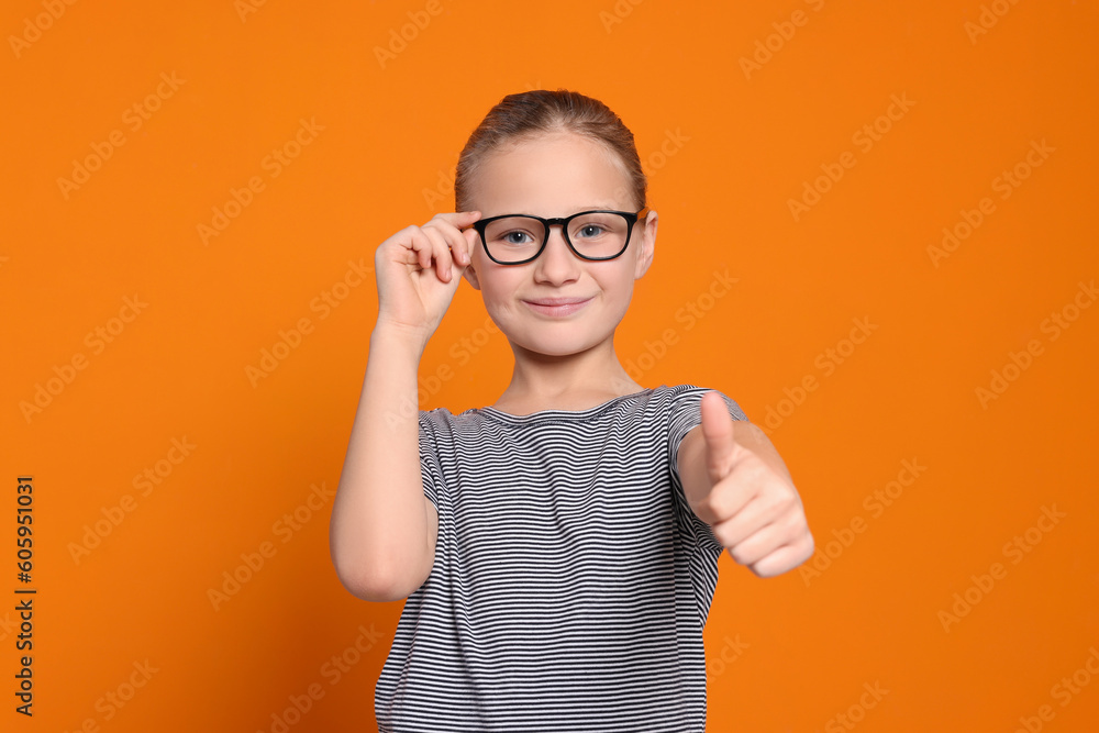 Cute girl in glasses showing thumb up on orange background Cute girl in glasses showing thumb up on orange background