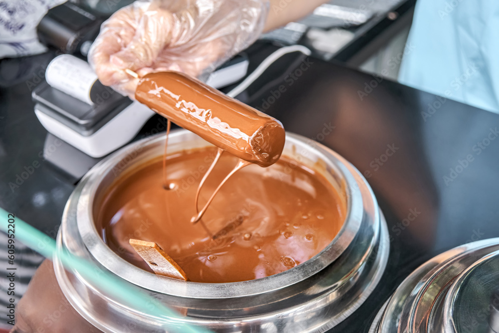 Salesman wearing plastic gloves dips ice cream on stick into hot chocolate. Process of popsicle making on special counter in city resort Salesman wearing plastic gloves dips ice cream on stick into hot chocolate. Process of popsicle making on special counter in city resort