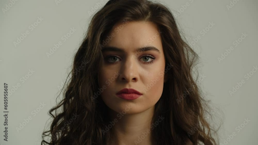 The long-haired brunette looks intently at the camera, and then looks away. Portrait shot of a young brunette against a gray wall. The long-haired brunette looks intently at the camera, and then looks away. Portrait shot of a young brunette against a gray wall.