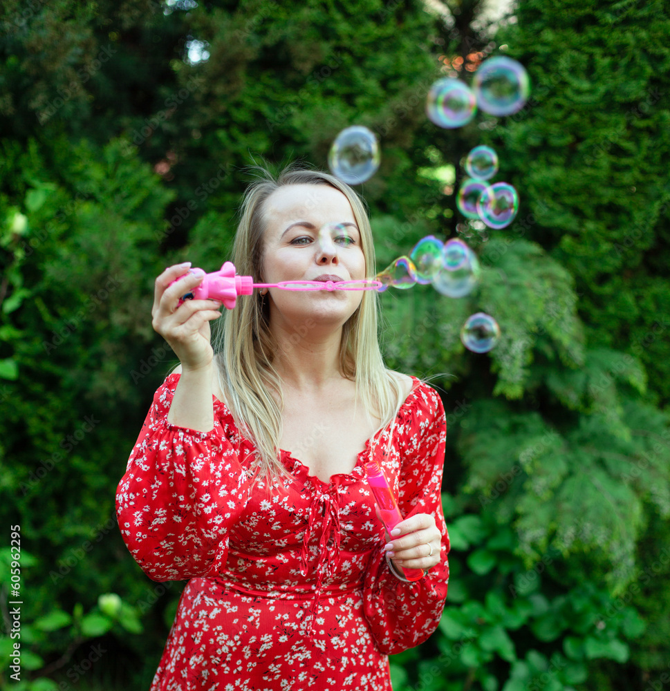 a woman in a red dress is playing with soap bubbles on the green lawn