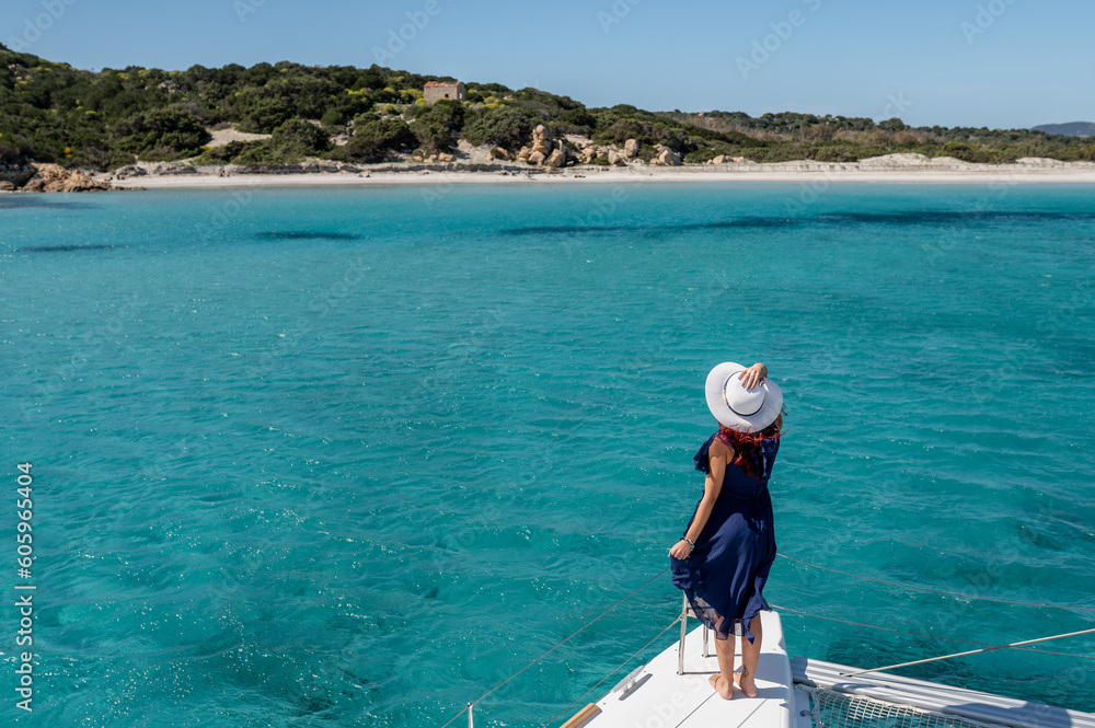 Back view of anonymous carefree female with hat standing on bow of catamaran and enjoying freedom while admiring seascape