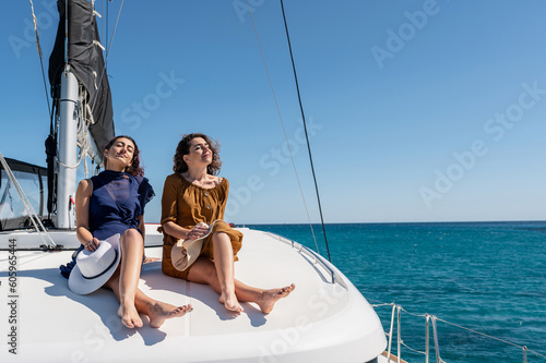 Carefree female friends sitting on catamaran and sunbathing while enjoying summer vacation on sunny day in sea © Pintau Studio