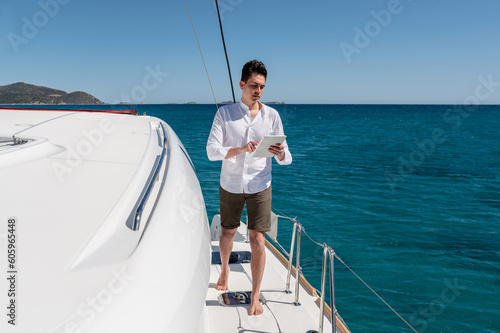 Calm male walking along deck of catamaran and surfing Internet on tablet while enjoying summer vacation