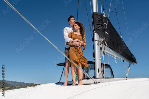 Loving couple embracing while standing on sailing catamaran in summer and enjoying vacation together © Pintau Studio